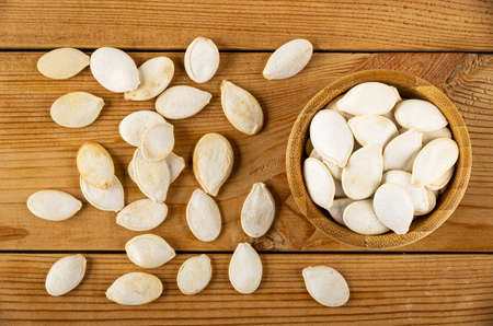 Scattered pumpkin seeds and bamboo bowl with pumpkin seeds on wooden table. Top view
