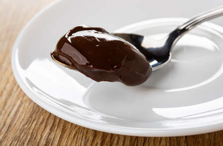 Melted chocolate cheese on metallic spoon in white glass saucer on wooden tableの写真素材