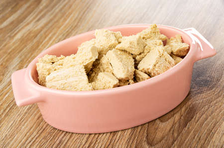 Pieces of peanut halva in oval pink bowl on wooden table