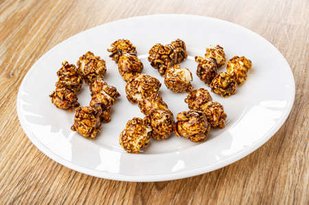 Few sweet brown popcorn with cocoa in white plate on wooden table