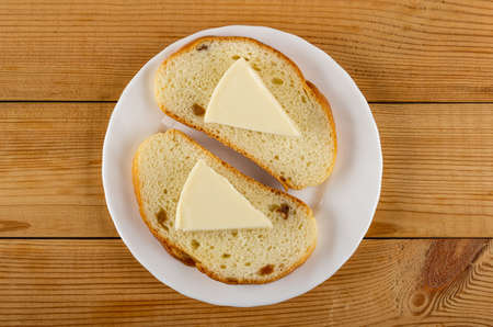 Slices of creamy cheese on slices of bread with raisin in white plate on wooden table. Top view