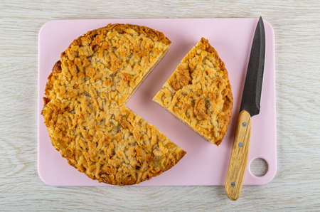 Shortbread pie with lemon jam, kitchen knife on pink cutting board on wooden table. Top view