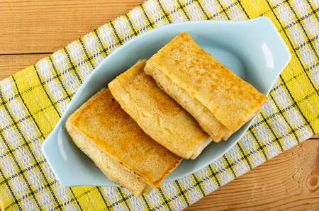 Three fried pancake rolls in blue plate on checkered napkin on wooden table. Top view