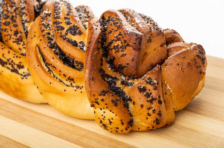 Close up of wicker sweet bun with poppy on bamboo striped cutting board