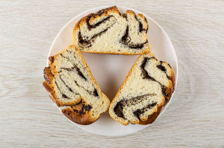 Three slices of wicker sweet bun with poppy in white plate on wooden table. Top view
