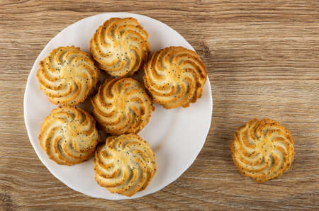 Shortbread cookies with poppy seeds in white plate, cookie on wooden table. Top view