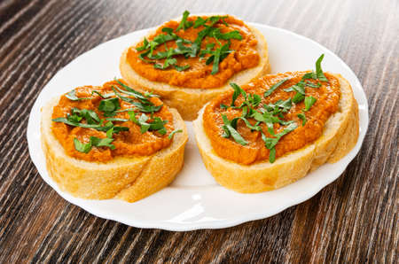 Sandwiches with squash caviar and parsley in white plate on dark wooden table