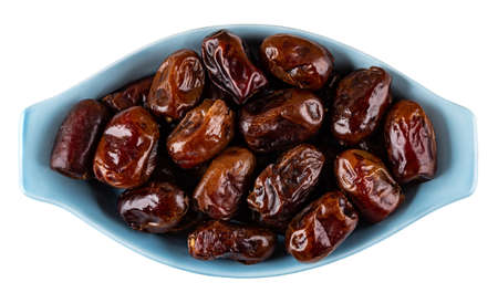 Heap of dried dates in glass blue bowl isolated on white background. Top view