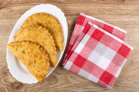 Three fried cheburek in glass white dish, checkered napkin on wooden table. Top viewの写真素材
