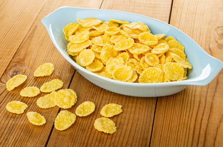 Scattered cornflakes, blue oval bowl with corn flakes on wooden table