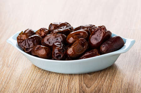 Heap of dried dates in glass blue bowl on wooden table