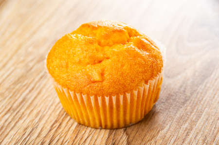 Single orange muffin on brown wooden table