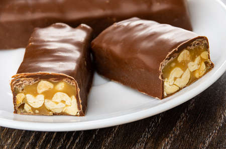 Close up of halves of chocolate bar with caramel and peanut in white plate on dark wooden table