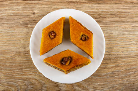 Three pieces of baklava with walnut in glass white plate on wooden table. Top view