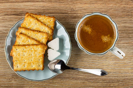 Crunchy cookies with sesame, pieces of sugar in saucer, coffee espresso in light-blue cup, spoon on wooden table. Top viewの写真素材