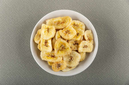 Banana chips in white glass bowl on gray table. Top viewの写真素材