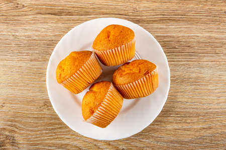 Lying on side orange muffins in white glass plate on brown wooden table. Top view