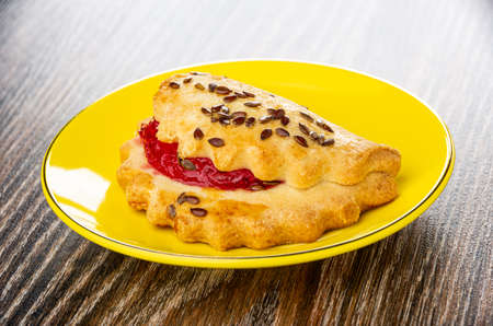 Shortbread cookie with raspberry jam and linseeds in yellow saucer on dark wooden tableの写真素材