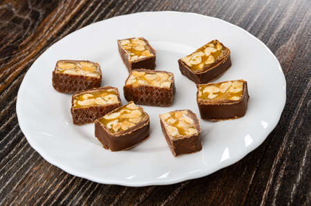 Small pieces of chocolate bar with caramel and peanut in white plate on dark wooden table