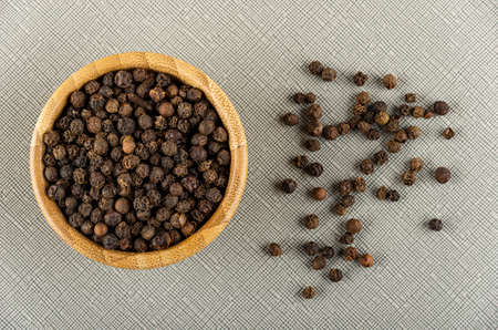 Bamboo bowl with peppercorn, scattered black pepper on gray table . Top viewの写真素材