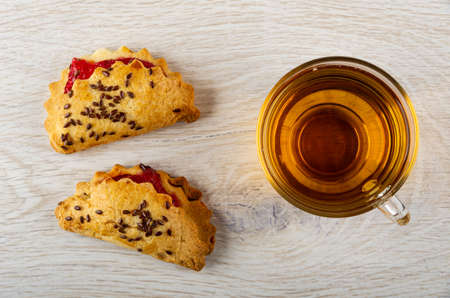Shortbread cookies with raspberry jam and linseeds, transparent cup with tea on wooden table. Top...