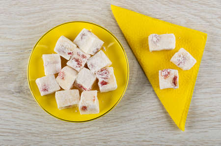 Rakhat-lukum with cherry in yellow saucer, rakhat-lokum on paper napkin on wooden table. Top view