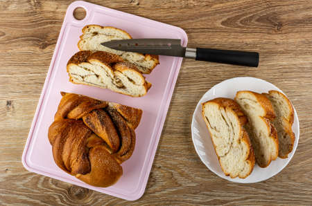 Pieces of wicker sweet bun with cinnamon on pink cutting board, kitchen knife, slices of bun in...
