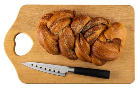 Wicker sweet bun with cinnamon and kitchen knife on wooden cutting board isolated on white...