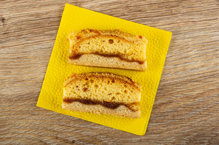 Slices of cake with apricot jam on yellow paper napkin on wooden table. Top view
