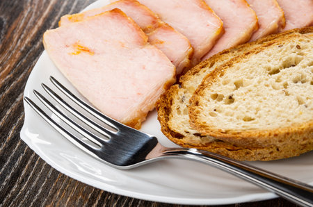 Slices of carbonnade, pieces of bread, fork in white dish on dark wooden tableの写真素材