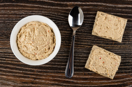 Cream-fish in white glass bowl, teaspoon, sandwiches with cream-fish on dark wooden table. Top viewの写真素材