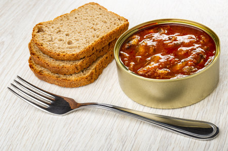 Slices of bread, opened metallic jar with sprat in tomato sauce, fork on wooden tableの写真素材