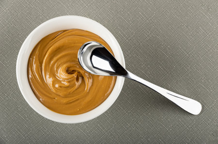 Teaspoon on white glass bowl with peanut butter on gray table. Top viewの写真素材