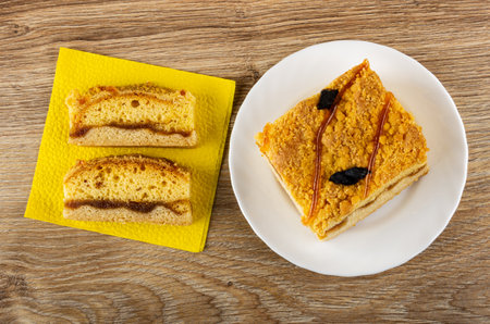 Slices of cake with apricot jam on yellow paper napkin, cake with jam and prune in white plate on...