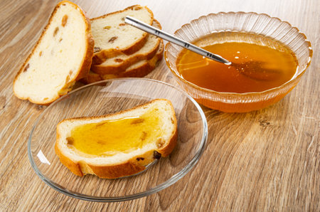 Slices of bread, teaspoon in glass bowl with honey, sandwich from rich bread with raisin and honey in transparent saucer on wooden tableの写真素材
