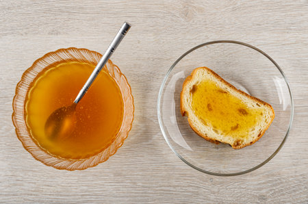 Teaspoon in transparent bowl with liquid honey, sandwich with honey in glass saucer on wooden table. Top viewの写真素材