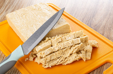 Kitchen knife on pieces of cutted peanut halva on orange plastic cutting board on wooden tableの写真素材