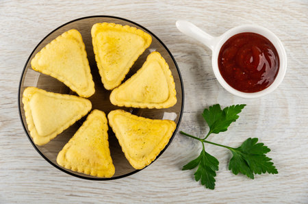 Few small savory pies in glass brown saucer, sauce boat with ketchup, leaves of parsley on wooden table. Top viewの写真素材