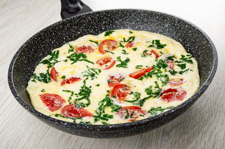 Omelette with tomato and parsley in frying pan on wooden table