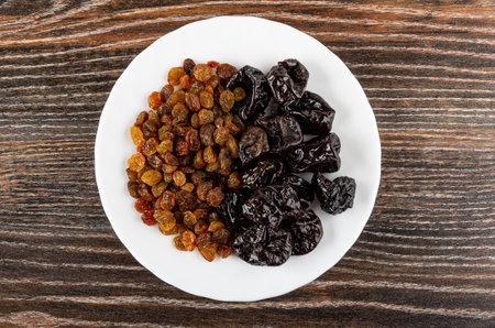 Raisin and dried black plums in white plate on dark wooden table. Top viewの写真素材