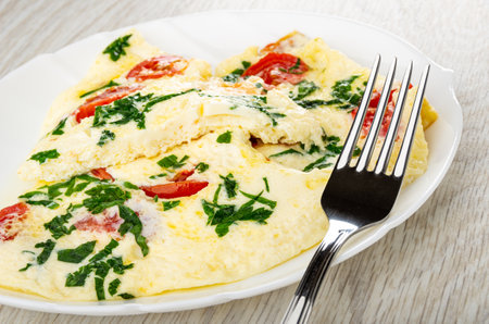 Pieces of omelette with tomato and parsley, fork in white glass dish on wooden table