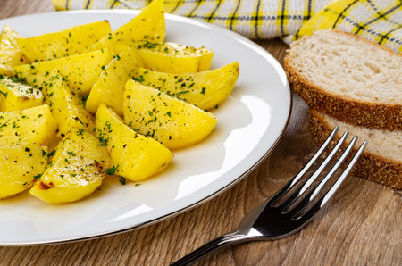Checkered napkin, pieces of bread, white plate with slices of fried potato, fork on wooden tableの写真素材