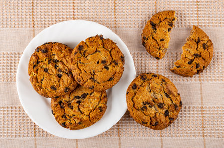Cookies with pieces of chocolate in white plate, pieces of broken cookie on checkered tablecloth. Top viewの写真素材