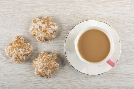Three gingerbread, coffee with milk in cup on saucer on light wooden table. Top view