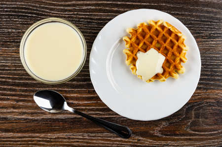 Transparent bowl with condensed milk, biscuit waffle poured condensed milk in white plate, teaspoon on dark wooden table. Top viewの写真素材