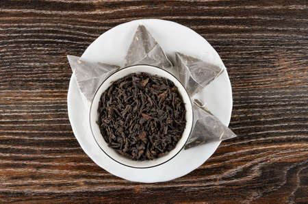 Leaf tea in glass bowl and tea bags with black tea in white plate on dark wooden table. Top viewの写真素材