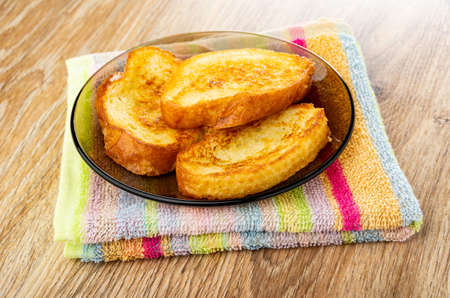 Fried toasts from wheat bread in brown saucer on folded striped napkin on wooden table