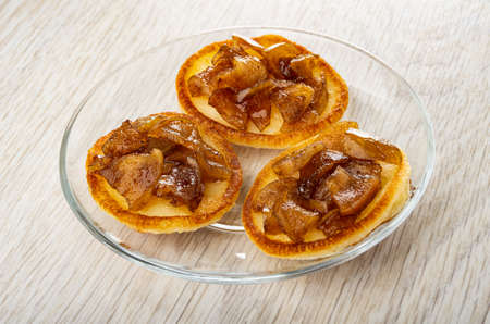 Three small homemade pancakes with jam from apple with cinnamon in transparent saucer on wooden tableの写真素材