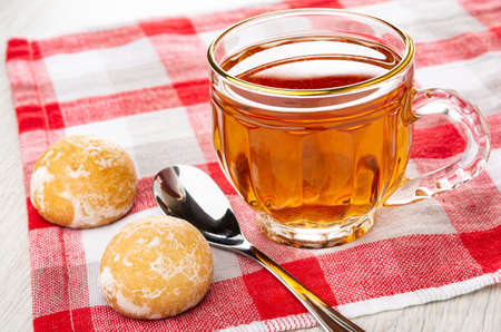 Brown gingerbread cookies, teaspoon, transparent cup with tea on checkered napkinの写真素材