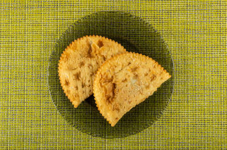 Two fried cheburek in transparent gray plate on yellow mat. Top view